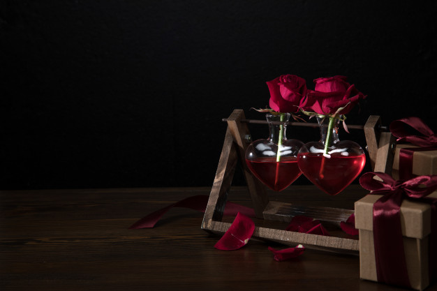 two-red-roses-in-heart-shaped-vases-on-wooden-stand-and-gift-boxes_20303-96